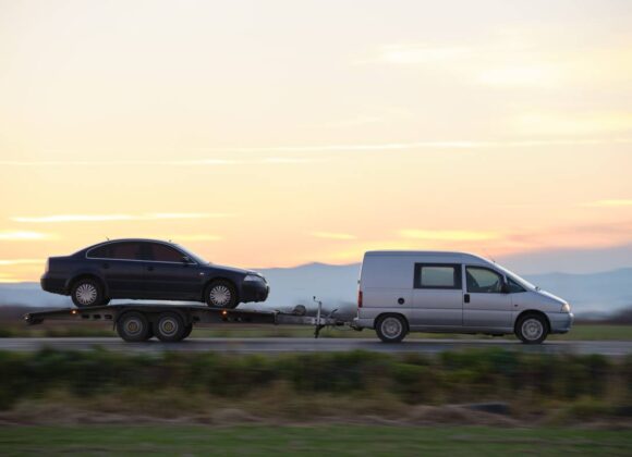 Tow truck vehicle with car transporting carrier trailer driving on highway in evening.